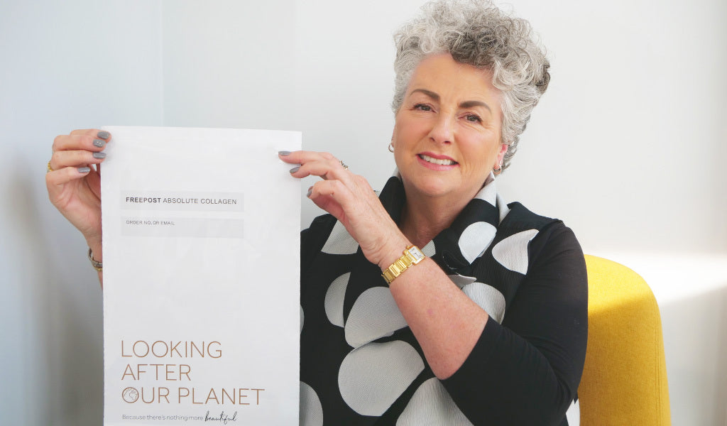 Photo of a white woman with short grey hair smiling at the camera and holding up a white plastic mailing bag.